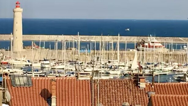 Un puerto deportivo con barcos amarrados, un faro y cielo despejado.