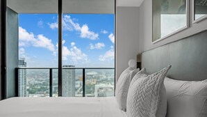 A bedroom with a large bed, white bedding, and a view of a cityscape through a balcony. - Sky-High Views & Pool – Steps from Miami Arena (Miami)