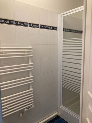 A bathroom with white tiled walls, a white radiator, and a glass shower enclosure.