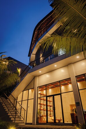 A modern building with a staircase leading to a balcony, large windows, and a palm tree. - Adiwana Unagi Riverfront (Mas)