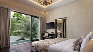 A hotel room with a large bed, a desk, a chair, a TV, and a bathroom. - Adiwana Unagi Riverfront (Mas)