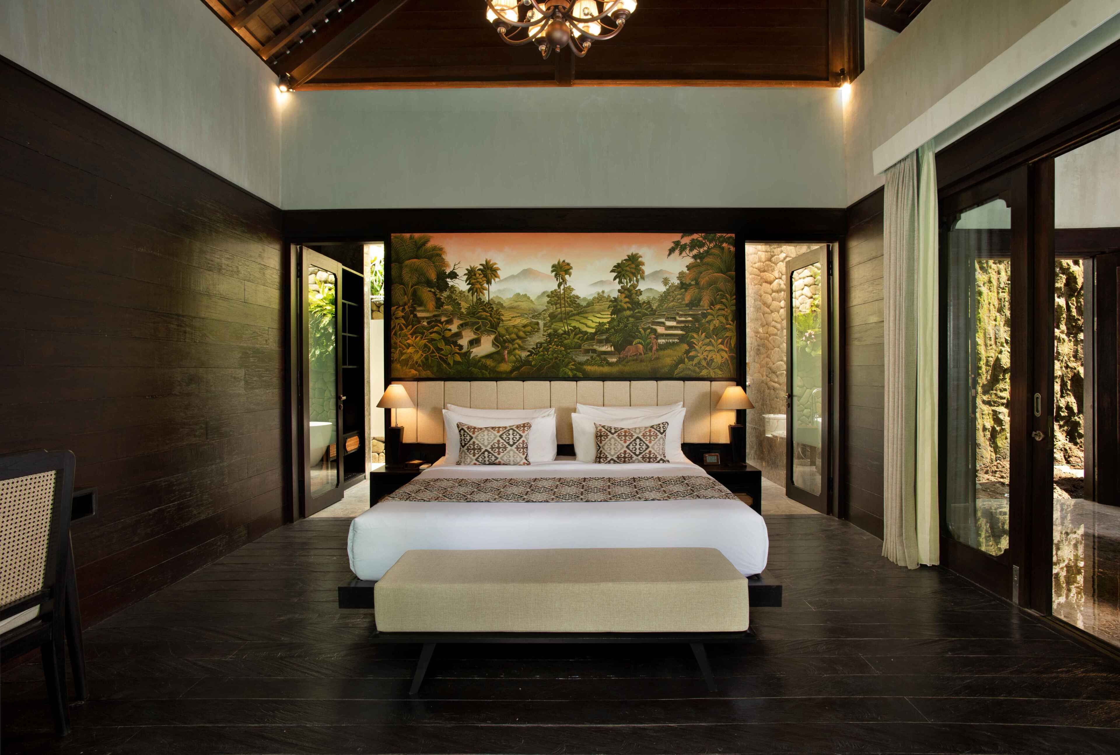 A large bed with a headboard, bedside lamps, and a view of a landscape painting.