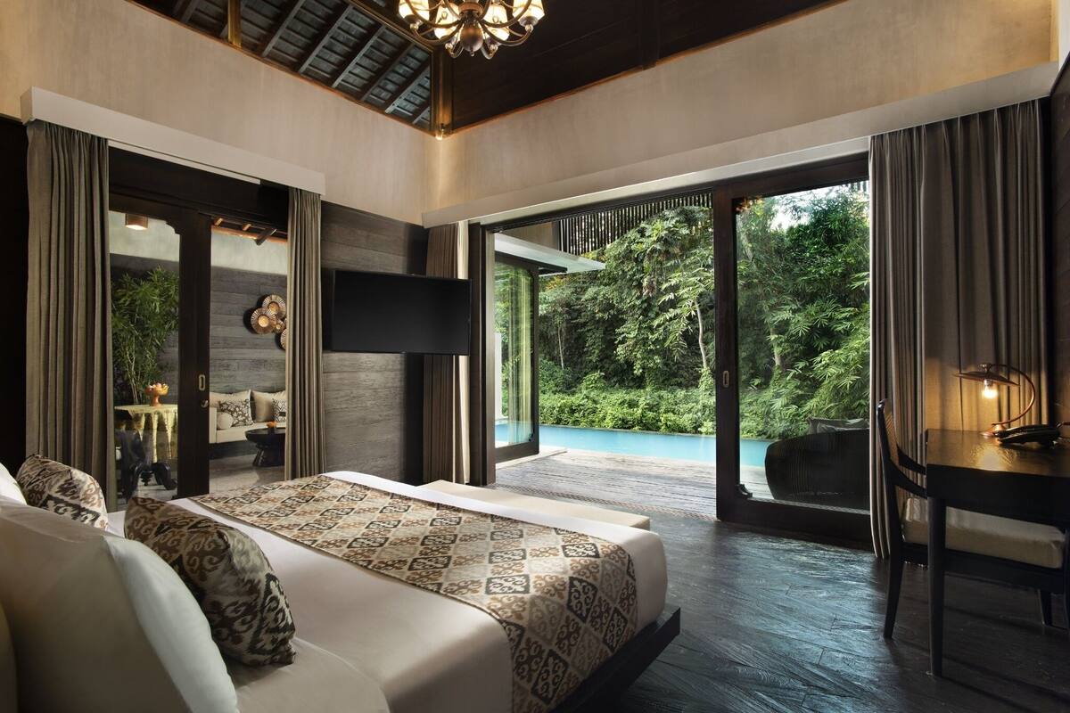 Une chambre moderne dotée d’un grand lit, d’un bureau et offrant une vue sur un jardin luxuriant et une piscine.
