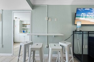 Una habitación con kitchenette, televisor montado en la pared y escritorio con silla.