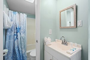 A bathroom with a shower curtain, a sink with toiletries, and a mirror.
