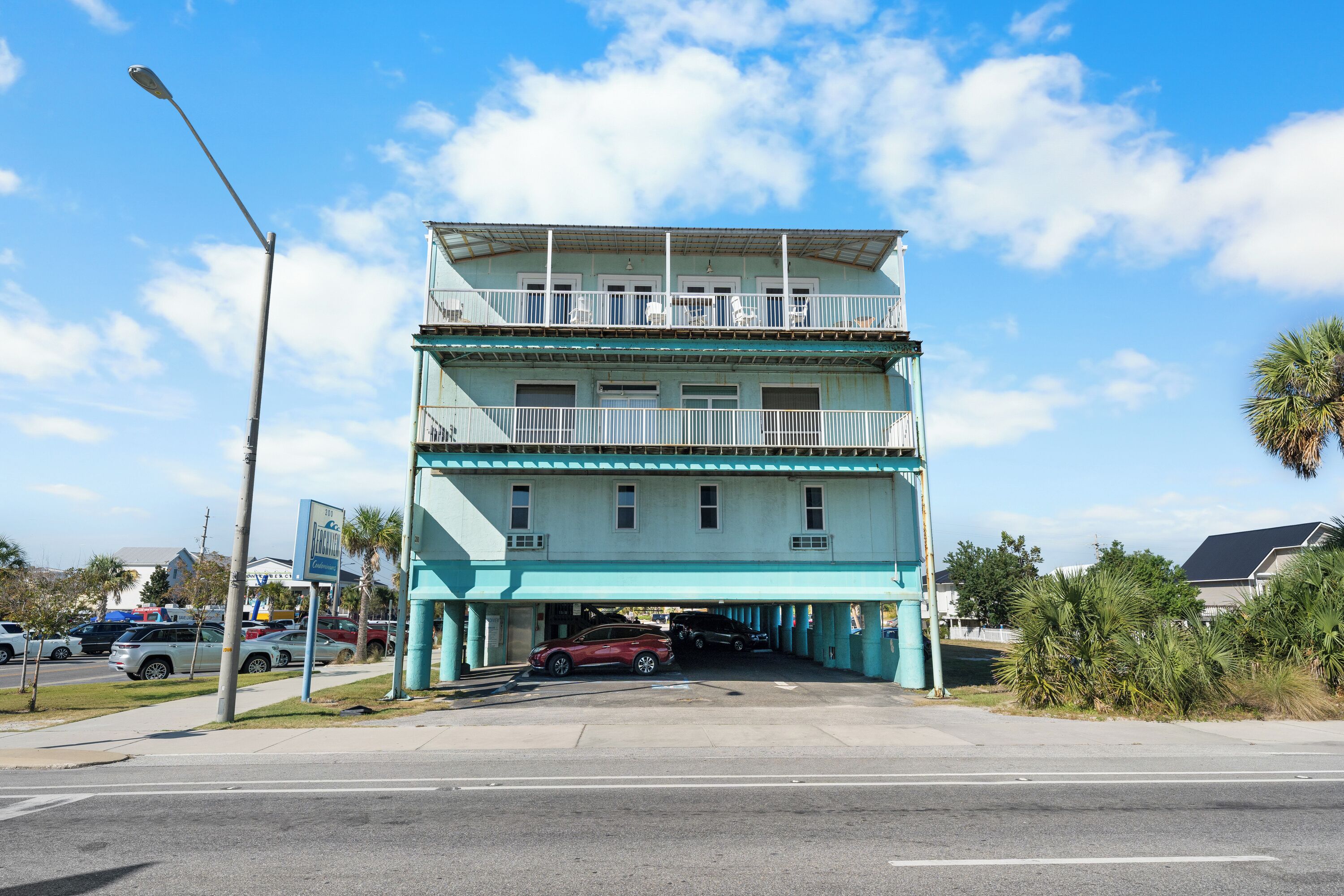 A multi-story building with balconies and a parking area in front.