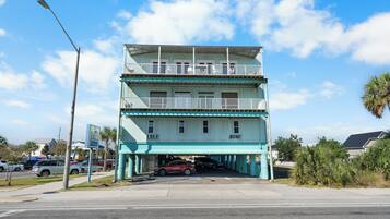 A multi-story building with balconies and a parking area in front.