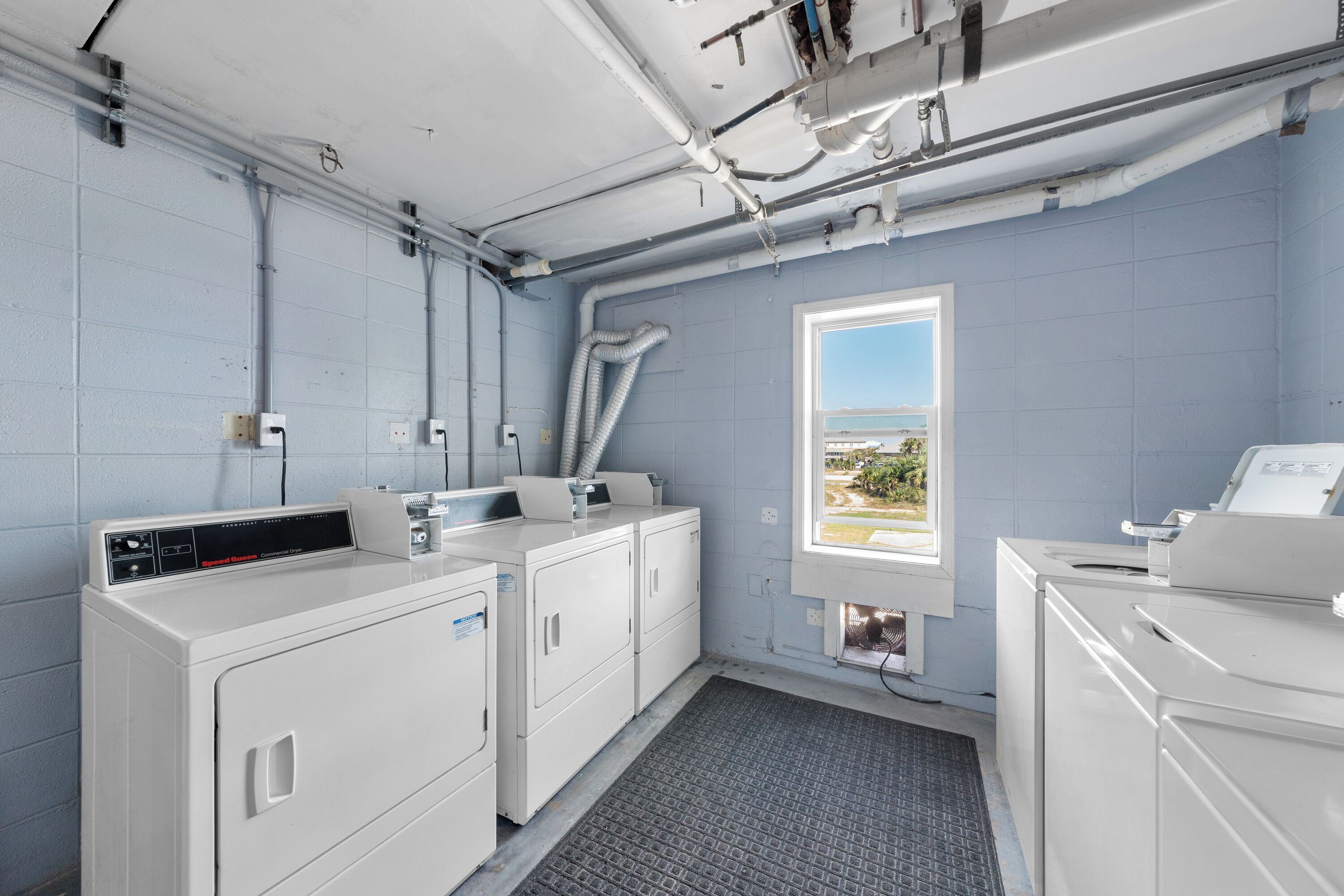 A laundry room with two washing machines, a dryer, and a window with a view.