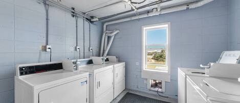 A laundry room with two washing machines, a dryer, and a window with a view.