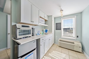 A kitchen with white cabinets, a microwave, a refrigerator, and a window with blinds.