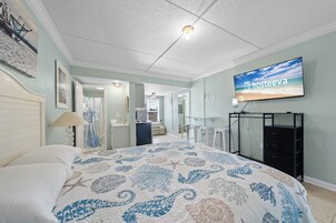 Un dormitorio con una cama, una televisión montada en la pared y un escritorio con una silla.