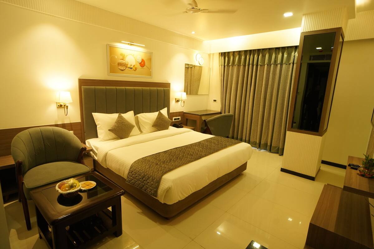 A hotel room with a large bed, a desk, a chair, a small table with a bowl and a plate, and a mirror.