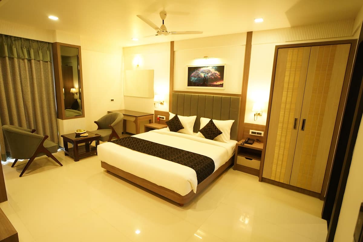 A hotel room with a large bed, a sitting area with a chair and a table, a wardrobe, and a ceiling fan.