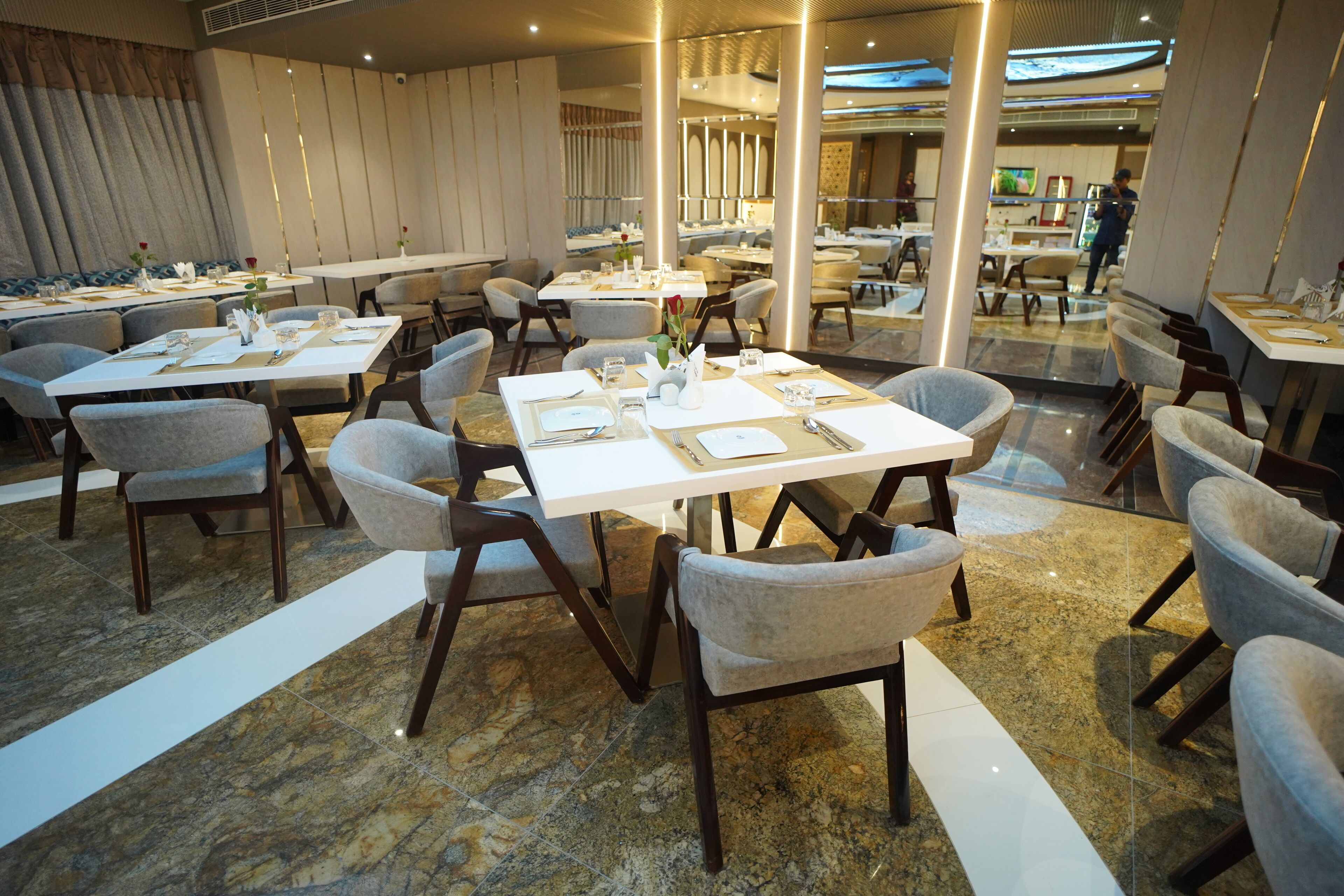 A modern dining area with marble flooring, white tables, and grey upholstered chairs.
