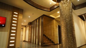 A modern hotel lobby with a large decorative pillar, a staircase, and a flat-screen TV mounted on the wall. - Hotel Square S (Varanasi)
