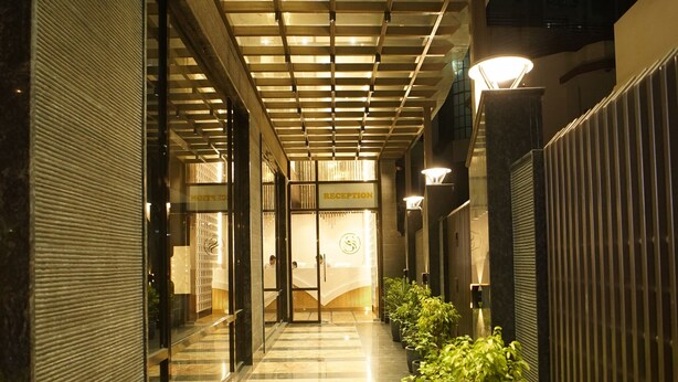 A corridor with a checkered floor, glass doors, and potted plants. - Hotel Square S (Varanasi)