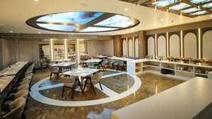 A spacious restaurant with a central circular seating area, high ceilings with skylights, and a modern interior design. - Hotel Square S (Varanasi)