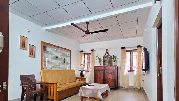 A spacious living room with a sofa, a small table, a ceiling fan, and a cabinet with a religious icon.