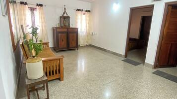 A spacious living room with a tiled floor, a ceiling fan, a wooden cabinet, and a potted plant.