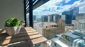 Une vue sur la ville, prise depuis une fenêtre d’un immeuble de grande hauteur, avec une plante en pot posée sur un banc en bois.