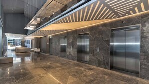 Un hall d’entrée moderne avec un sol en marbre, un ascenseur en verre et un design contemporain au plafond.