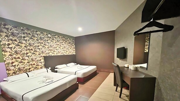 Hotelkamer met twee bedden, een bureau, een stoel, een televisie en een wand met een bloemenpatroon.
