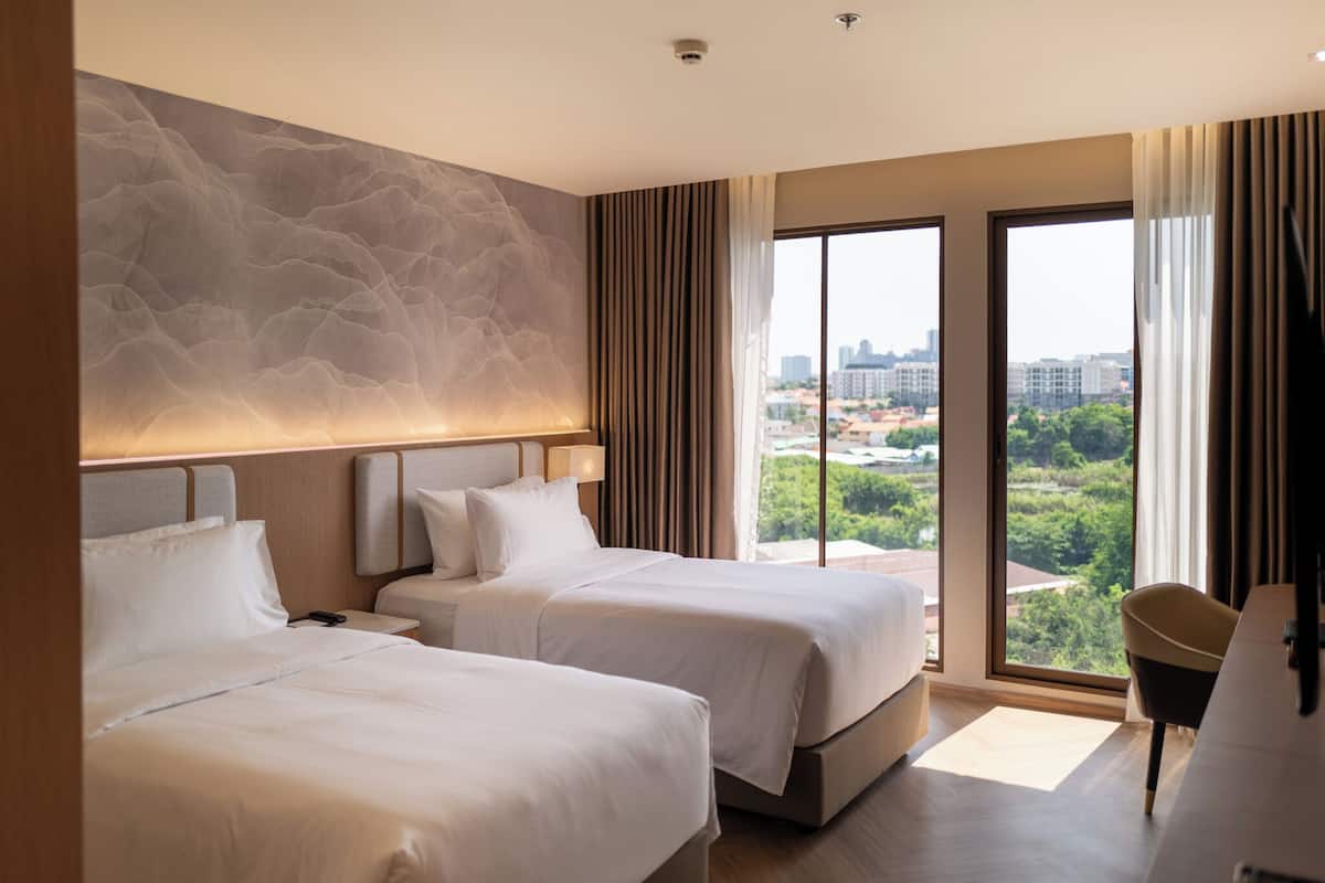 Een moderne hotelkamer met twee bedden, een groot raam met uitzicht op de stad en een gestructureerde wand.