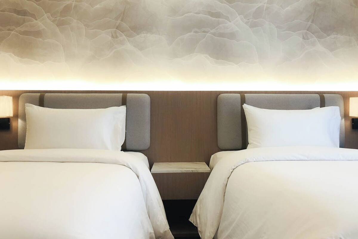 Een hotelkamer met twee bedden, een houten hoofdbord, een wandlamp en een gestructureerd wandontwerp.