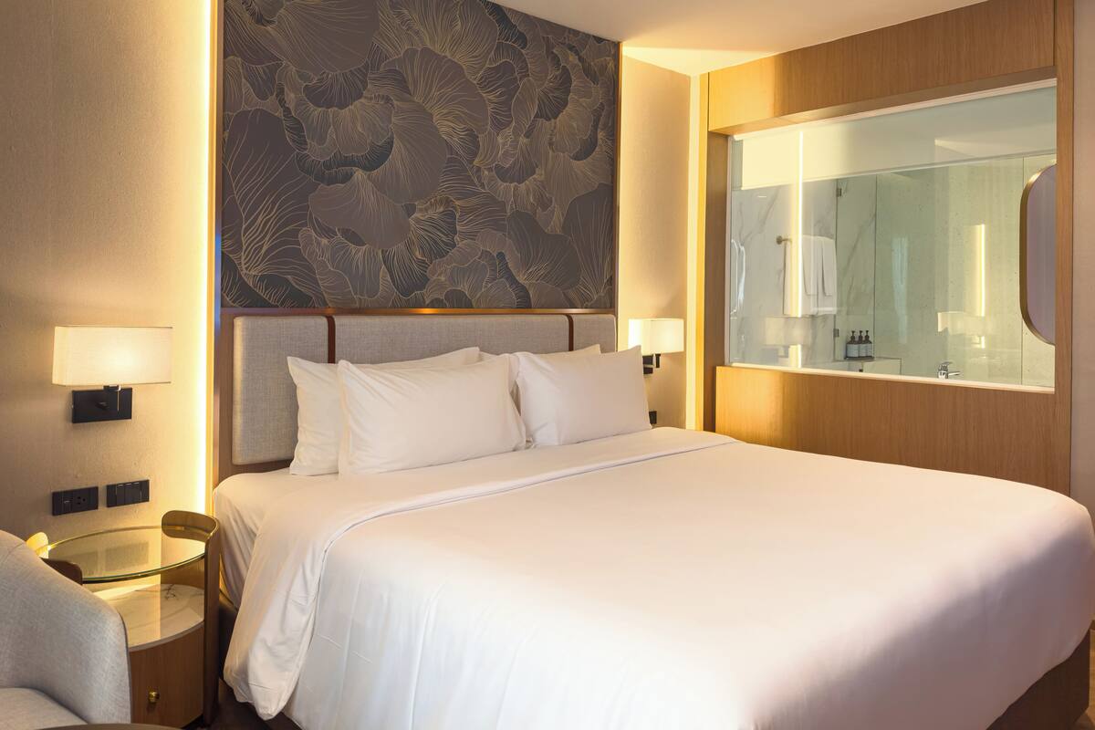 Hotelkamer met een groot bed, een glazen tafeltje, een stoel, een wand met bloemenprint en een spiegel.