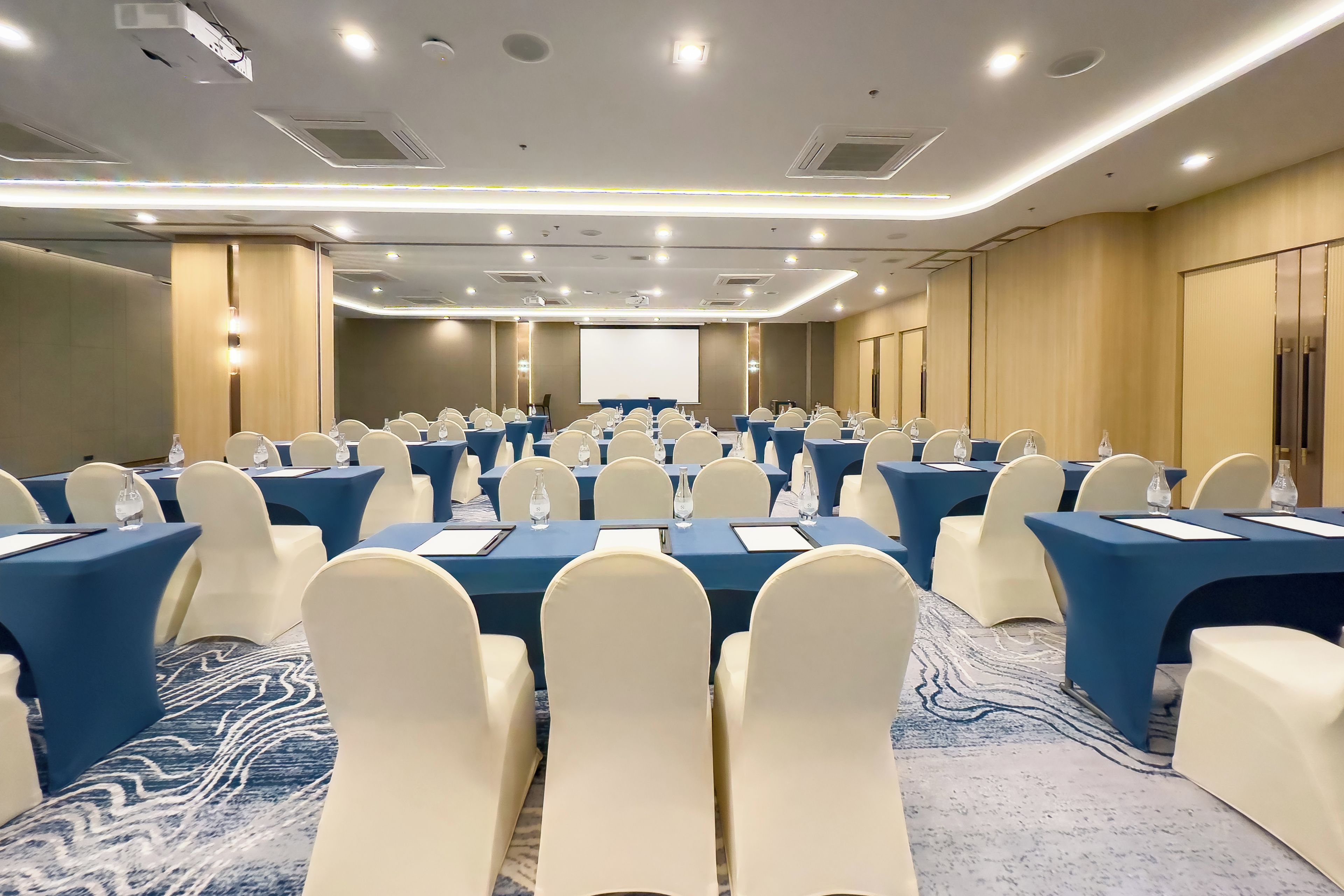 A conference room with rows of tables and chairs, equipped with water bottles and nameplates.