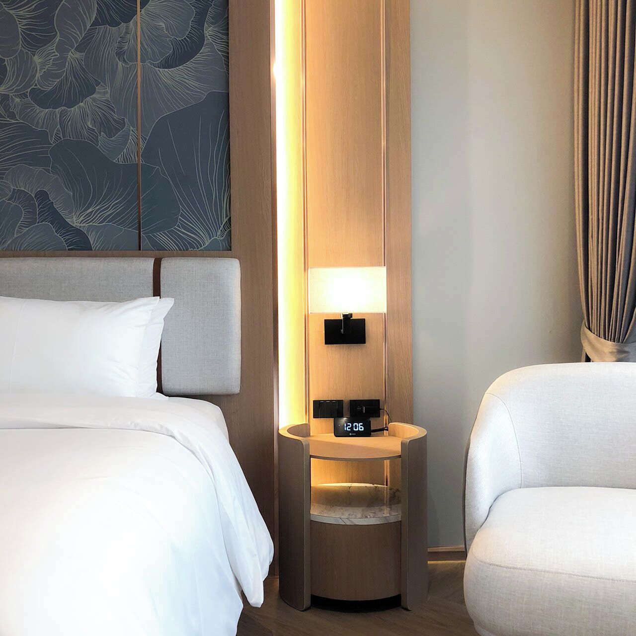 Ein Hotelzimmer mit einem Bett, einem Nachttisch mit Lampe und einer Wand mit Blattmuster.