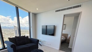 A modern living room with a large window, a flat-screen TV, and a view of a cityscape. - Sky High Luxury - 59th Floor at Ocean (Surfers Paradise)