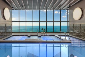 A large indoor swimming pool with a view of the ocean through large windows.