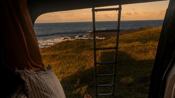 A bed with striped pillows, a view of the ocean through a window, and a ladder leaning against the window frame. - VAN Longani (Le Tampon)