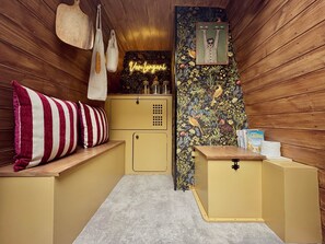 A cozy room with wooden walls, a small kitchenette, a bench with a striped pillow, and a neon sign on the wall. - VAN Longani (Le Tampon)