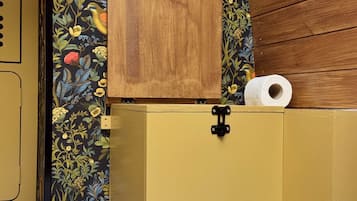 A yellow cabinet with a wooden box on top, a roll of toilet paper, and a floral wallpaper.