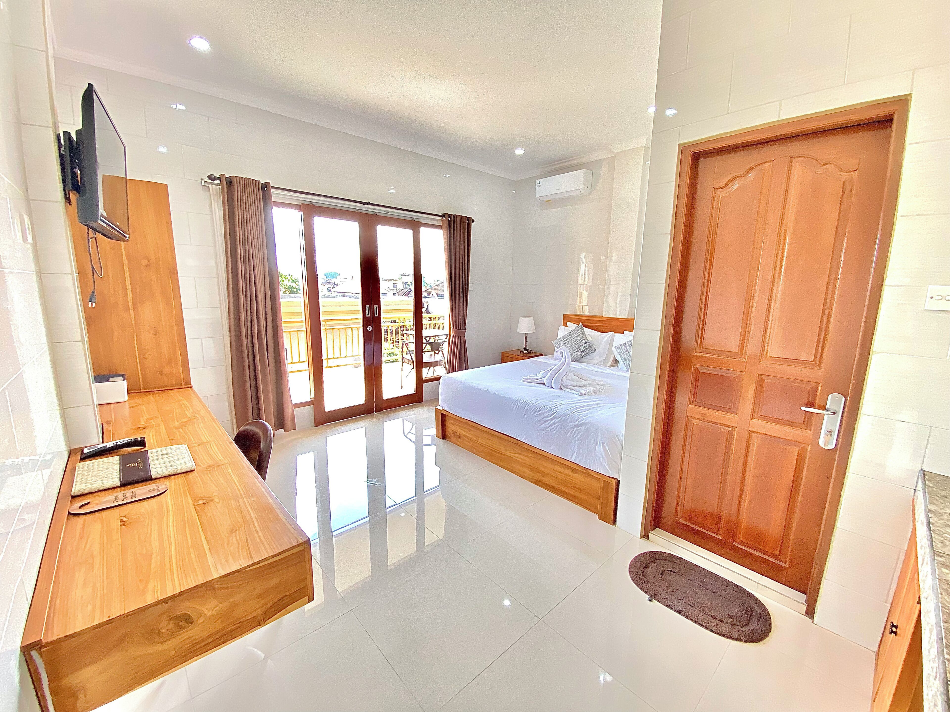 A hotel room with a bed, a desk, a TV, a sliding glass door to the balcony, and a wooden door.