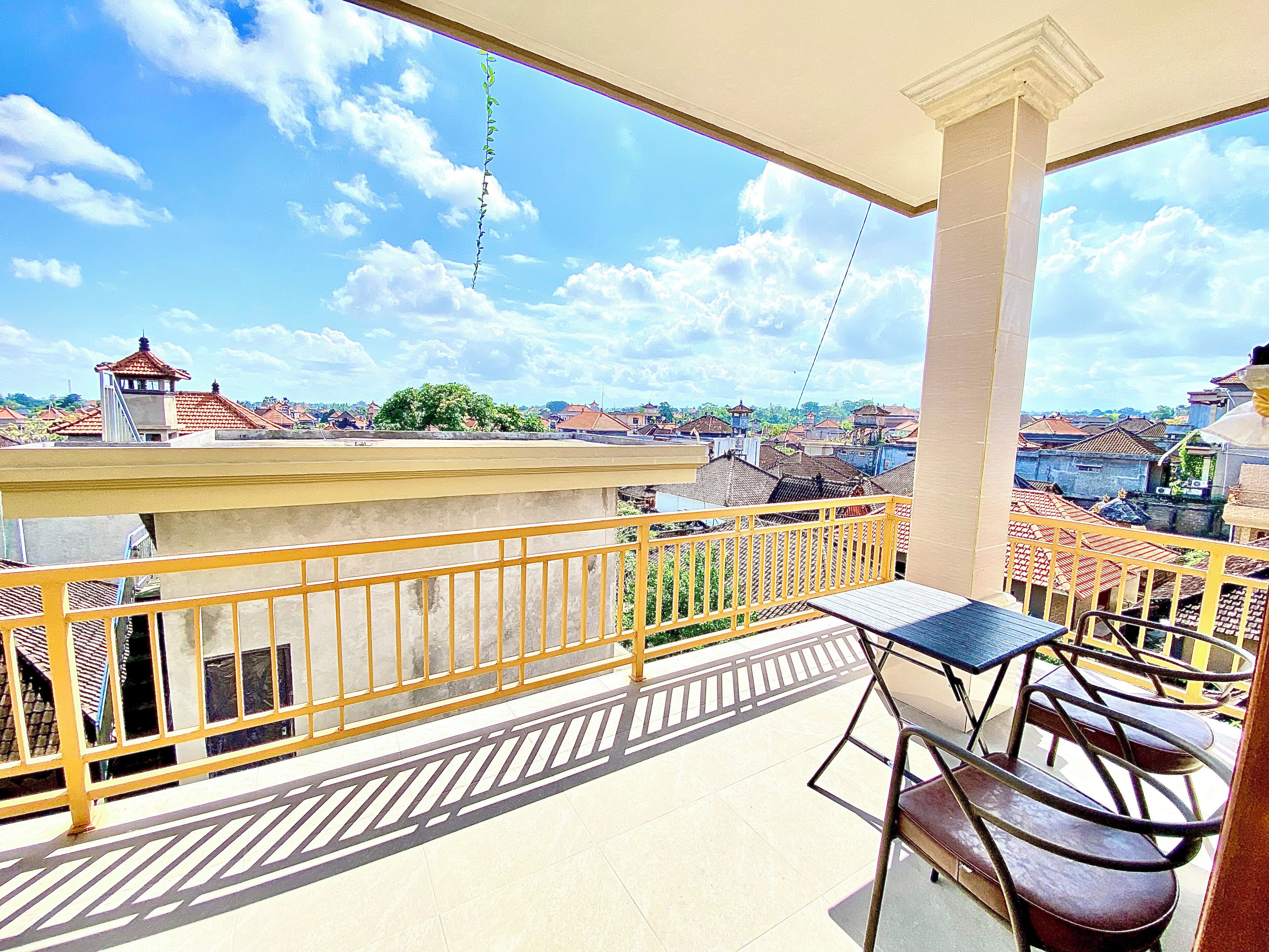 A balcony with a table and chairs, overlooking a residential area with traditional buildings and a clear sky.