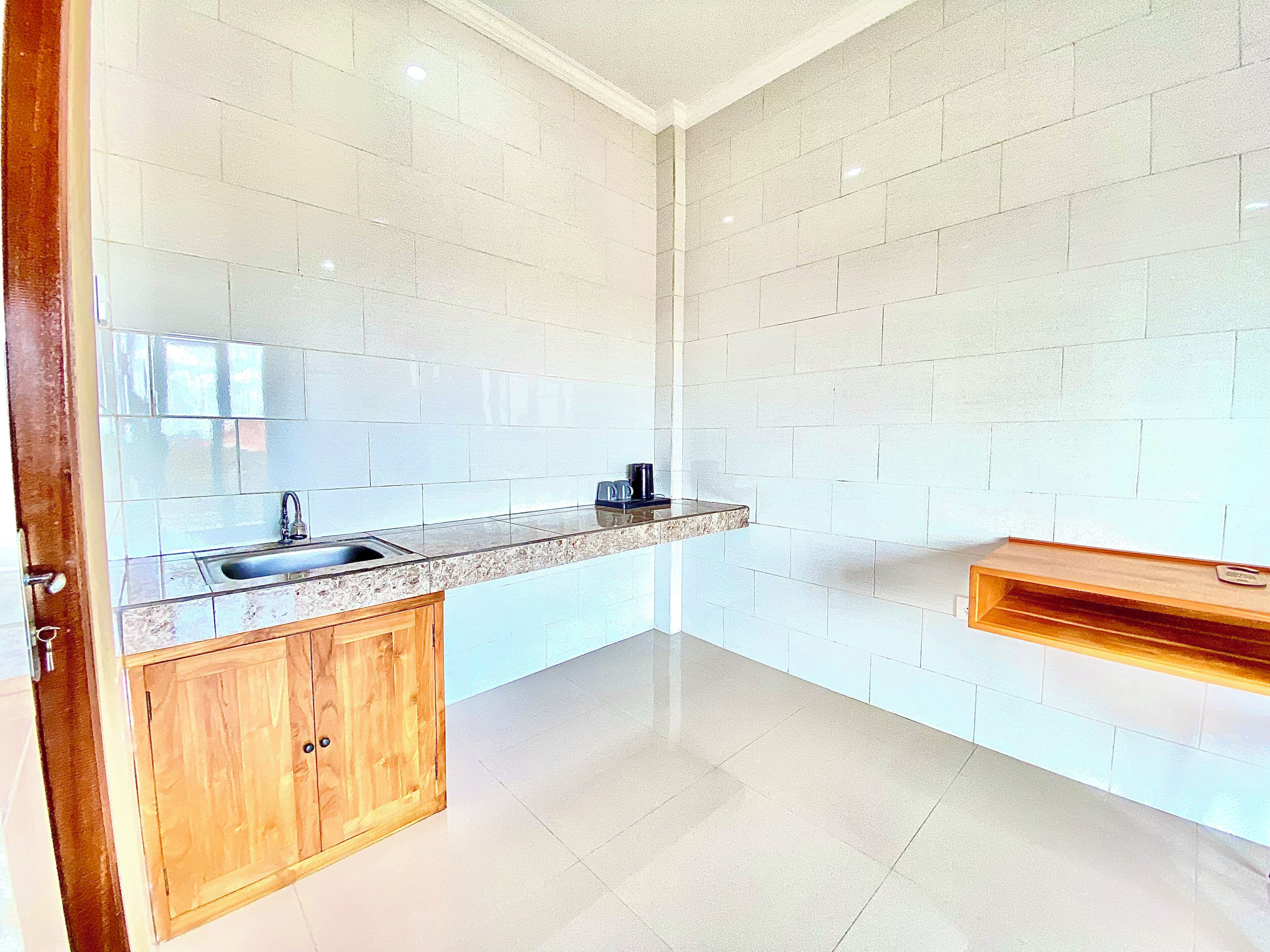 A kitchen with a sink, wooden cabinets, a countertop, and a wooden shelf.