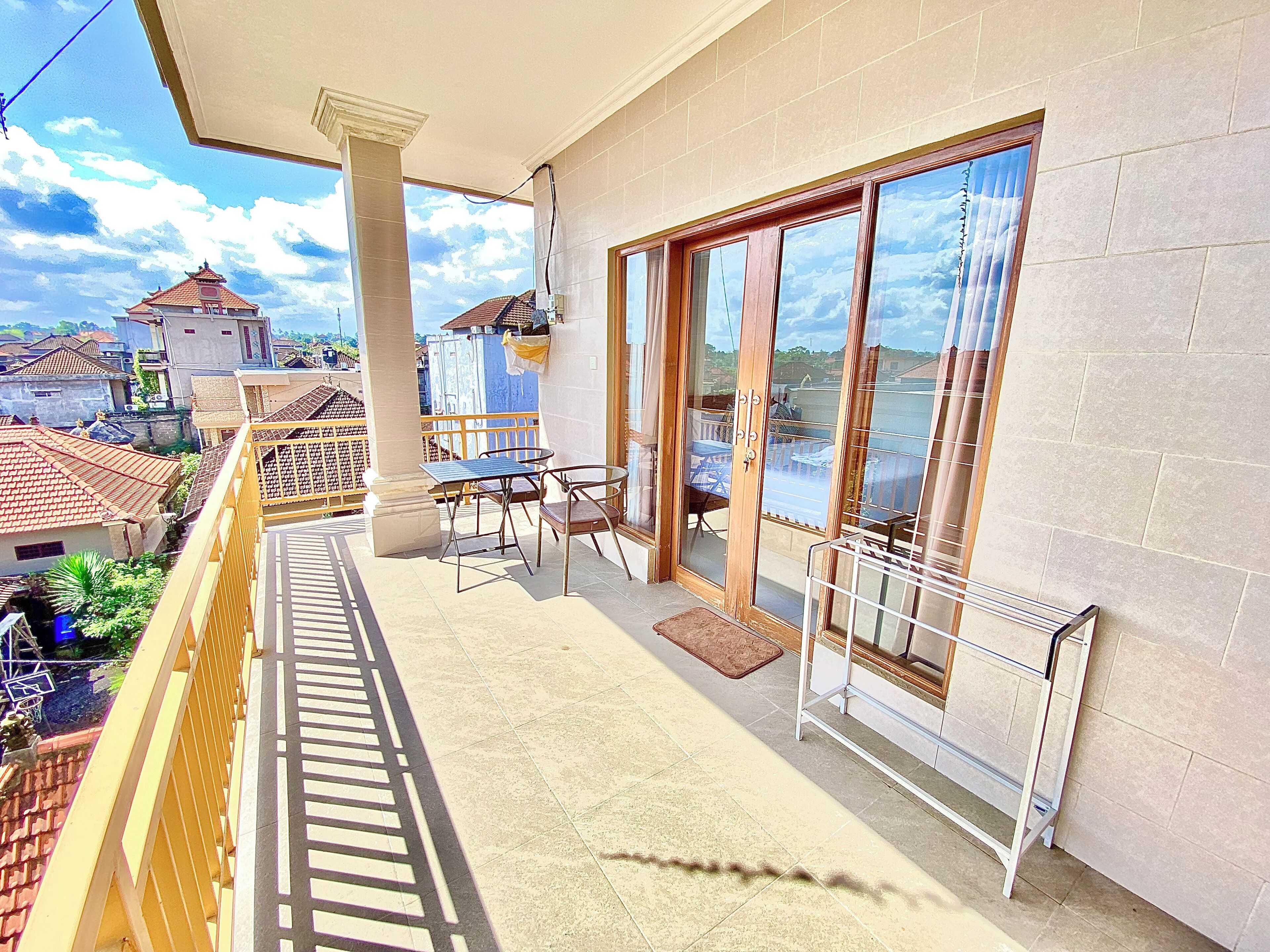 A balcony with a table and chairs, a view of the sea, and a building with a tiled roof in the background.