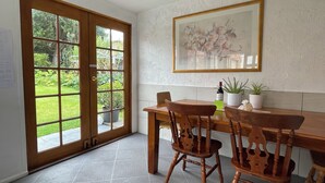 A dining area with a wooden table and chairs, a framed floral artwork on the wall, and a view of a garden through a glass door. - Garden View Entire Self Contained Guesthouse (Engadine)