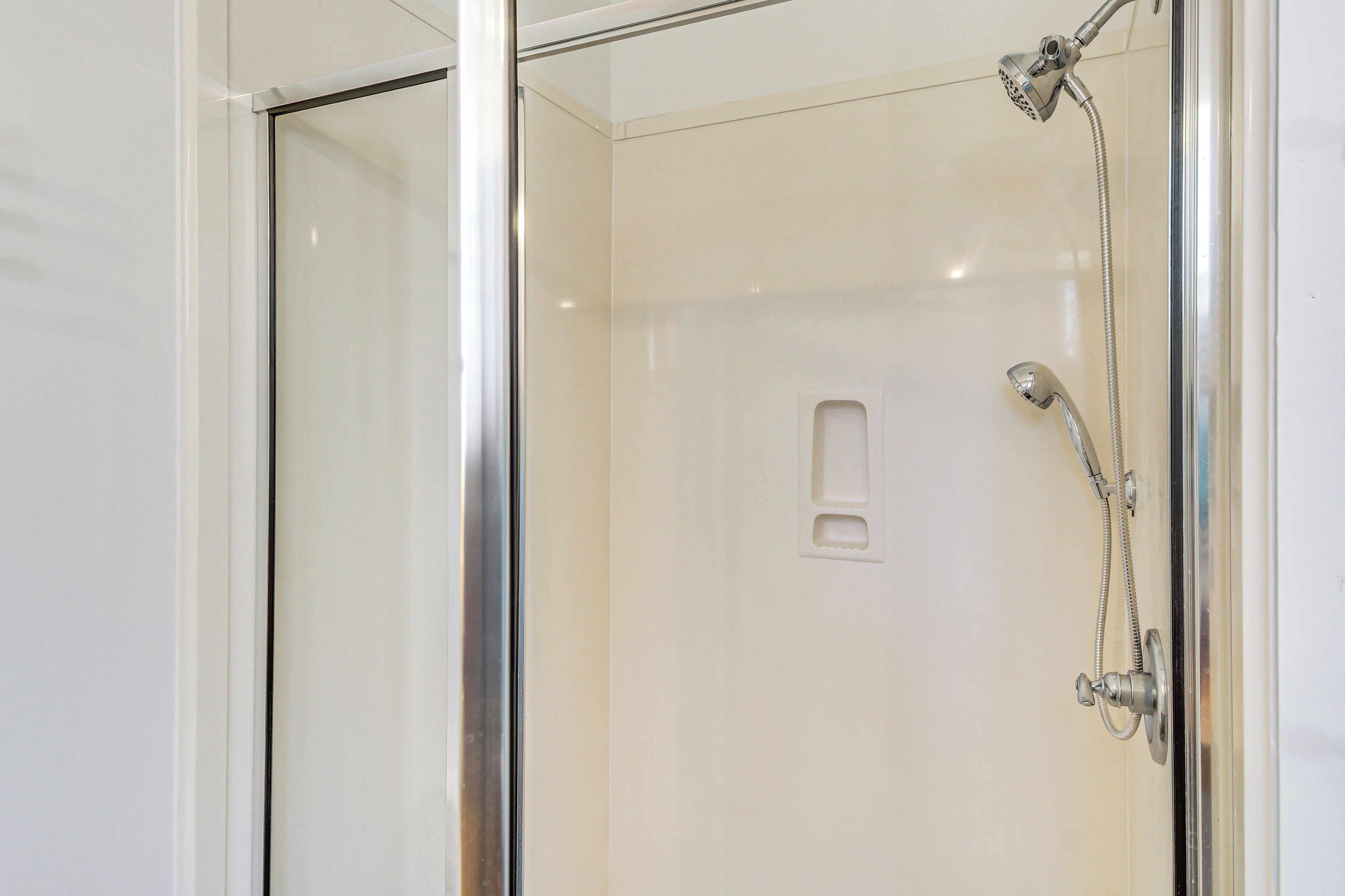 Une cabine de douche fermée par des parois en verre, dotée d’un pommeau de douche à main et d’un robinet fixé au mur.