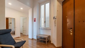 Une chambre d’hôtel avec un plancher en bois, une grande porte en bois, une petite table, une chaise et une fenêtre avec des stores.