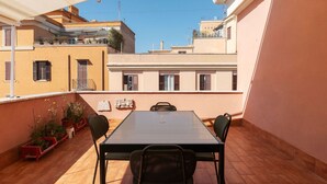Une terrasse sur le toit, avec une table et des chaises, des plantes en pot et une vue sur les bâtiments voisins.