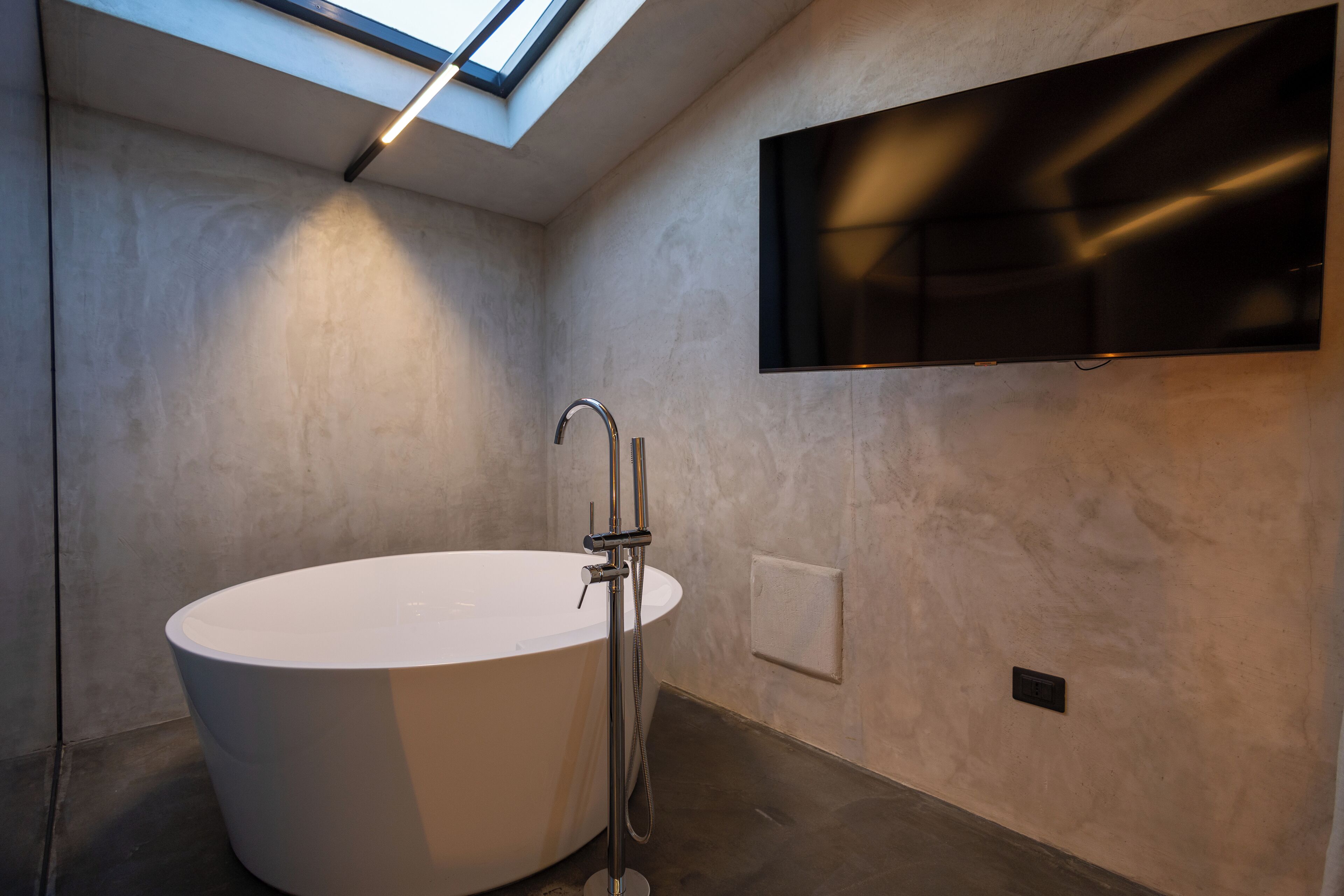 Une salle de bain moderne avec une baignoire sur pieds, un téléviseur fixé au mur et une lucarne.