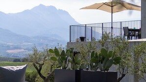 Un patio exterior con vistas a montañas, una mesa con sillas y un paraguas grande.