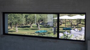 Vista a través de una ventana de un jardín con mesas al aire libre y árboles.