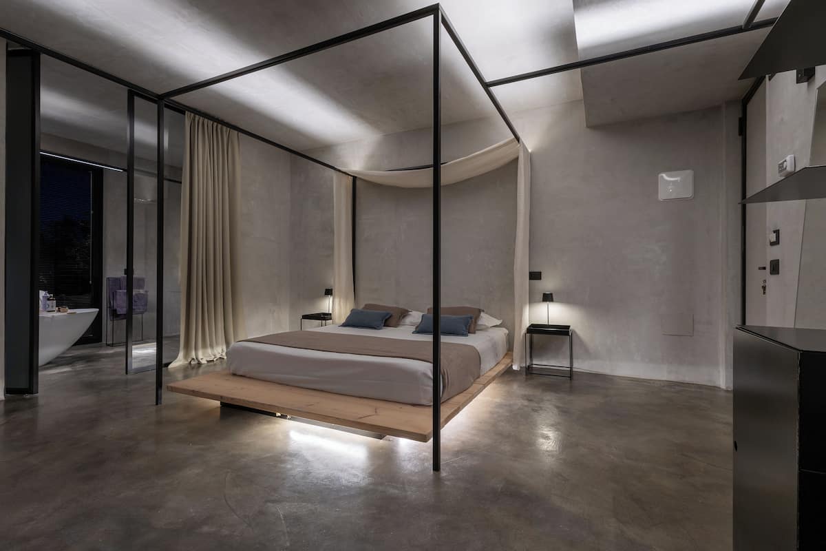 Un dormitorio moderno con diseño minimalista, que presenta una cama con estructura de madera, una partición de vidrio y vistas a la ciudad de noche.