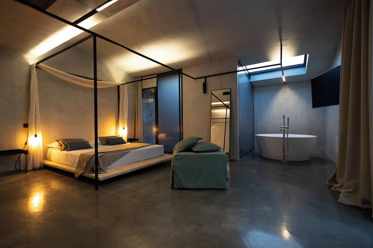 Un dormitorio moderno con cama con dosel, una zona de estar y una bañera independiente.