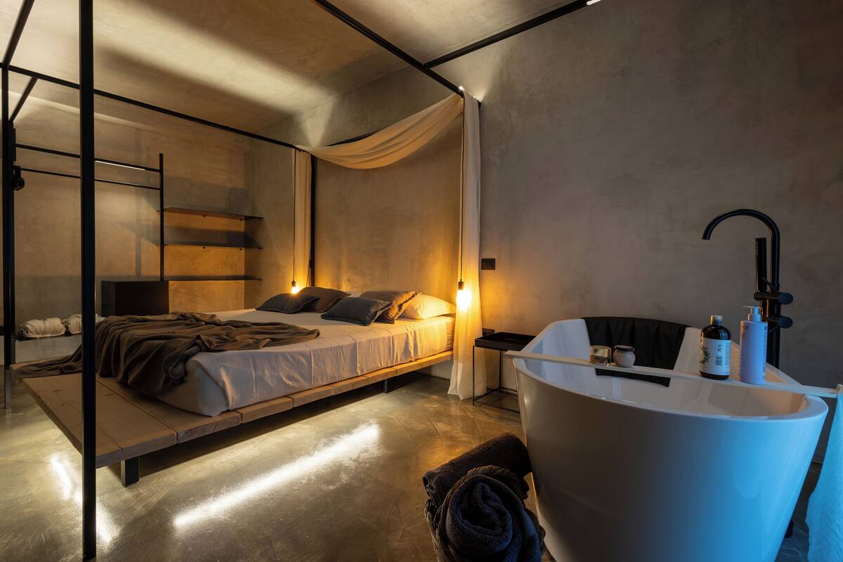 Un dormitorio moderno con cama, mesita de noche y una bañera grande.